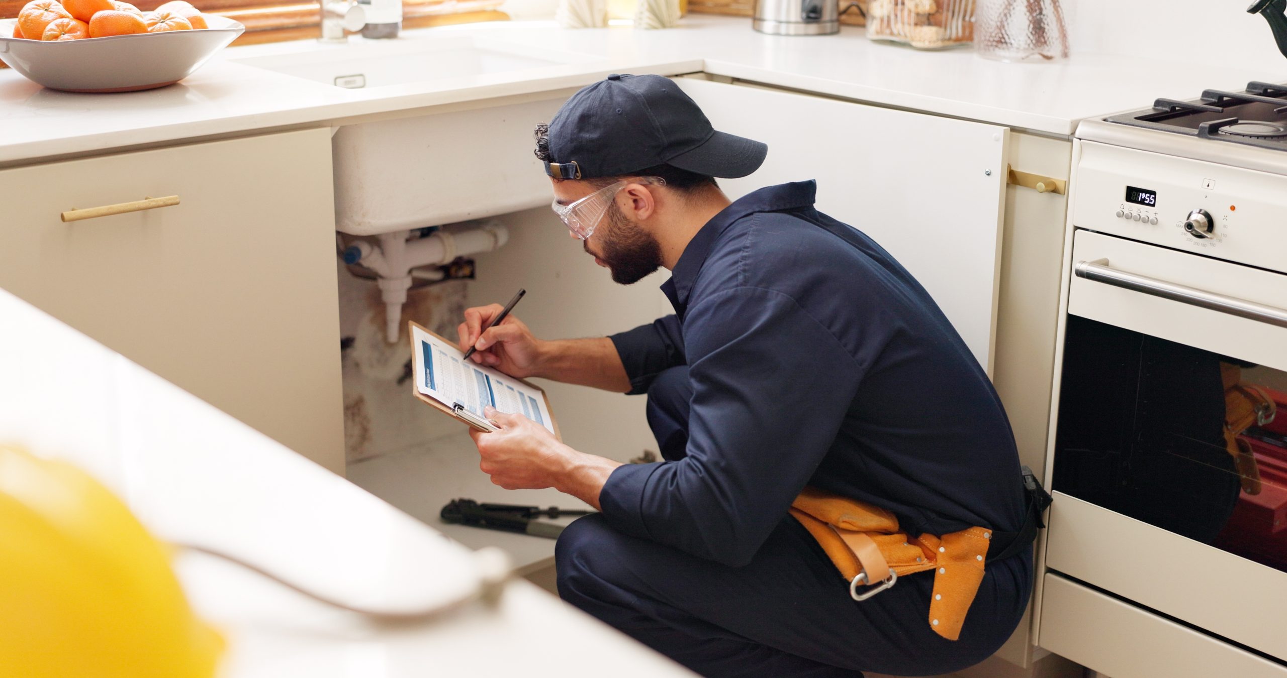 Plumber in residential kitchen writing on clipboard